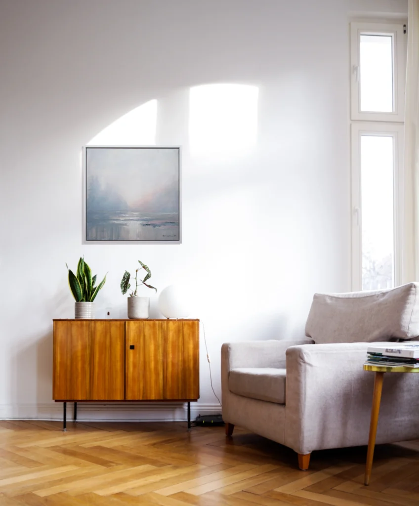 Soft Dawn original framed artwork displayed above a wooden cabinet in a calm sunlit living room.