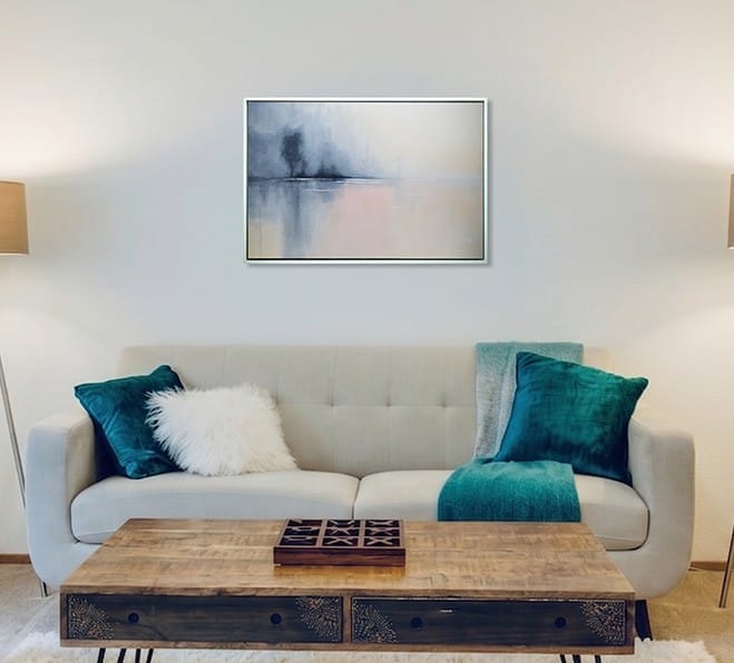 Whispers of Dawn original framed artwork displayed above a sofa with blue-green accent pillows in a contemporary living room.