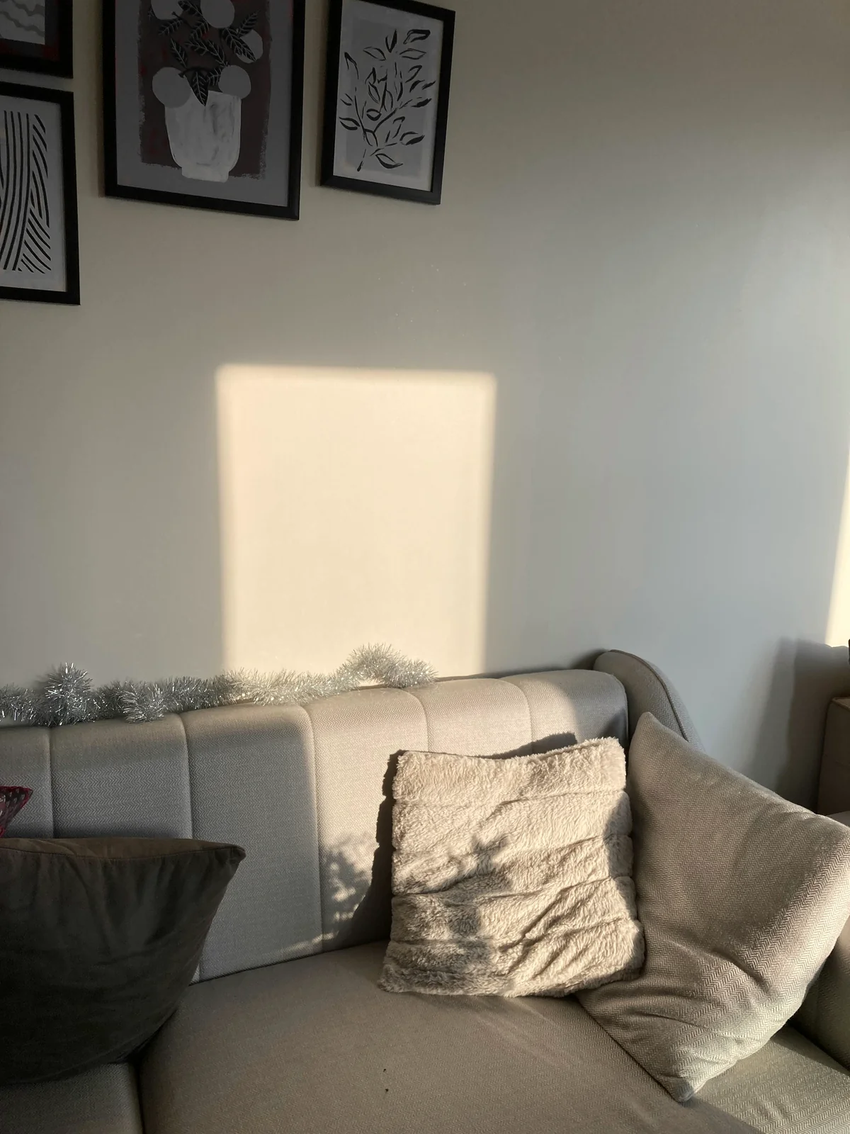 A wall the body finds first — soft afternoon light landing on it, framed prints sitting quietly in the upper edge of the room.