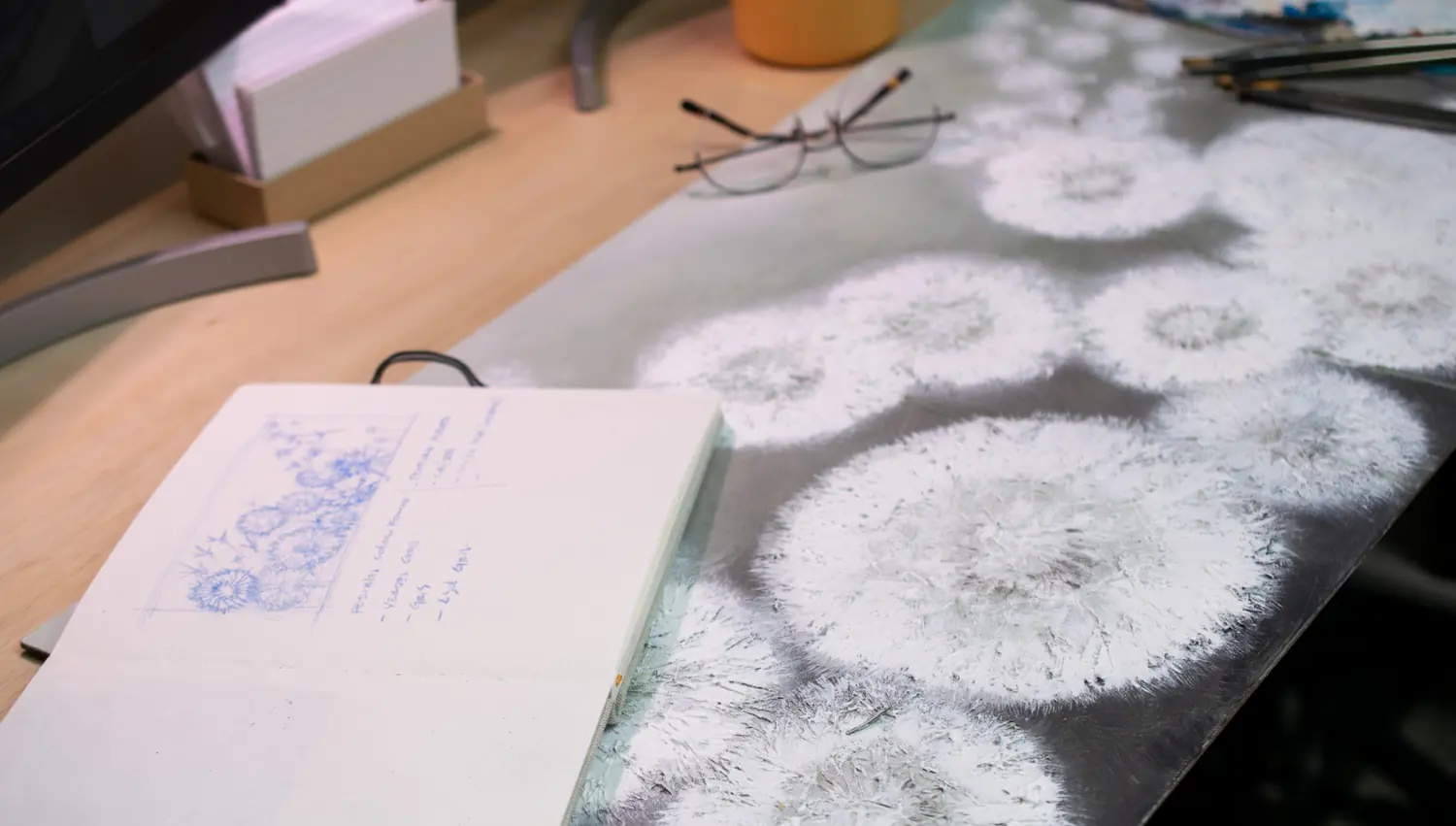 Textured floral artwork surface beside a sketchbook on the studio bench